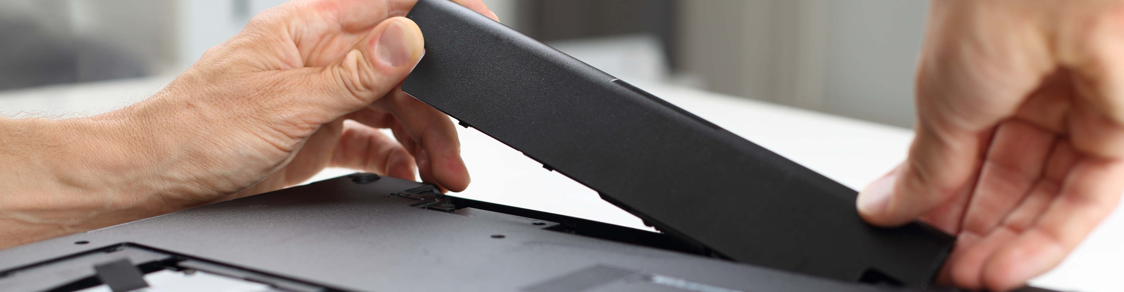 Egy férfi két kézzel behelyezi az akkumulátort a laptop aljába Egy férfi két kézzel behelyezi az akkumulátort a laptop aljába