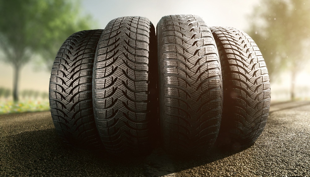 Čelní pohled na čtyři pneumatiky pro osobní auto srovnané vedle sebe na asfaltové cestě