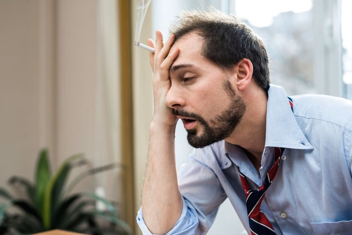 Bărbat epuizat și stresat, cu o țigară în mână, înainte de începerea unei cure de detoxifiere