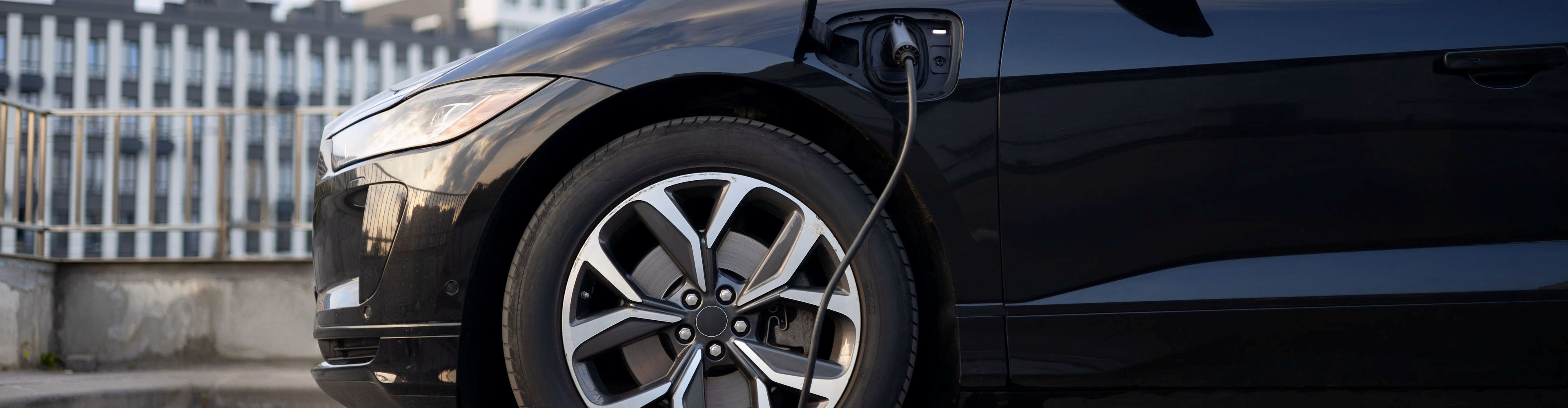 Vedere laterală a unei mașini electrice negre, parcată și conectată la încărcător