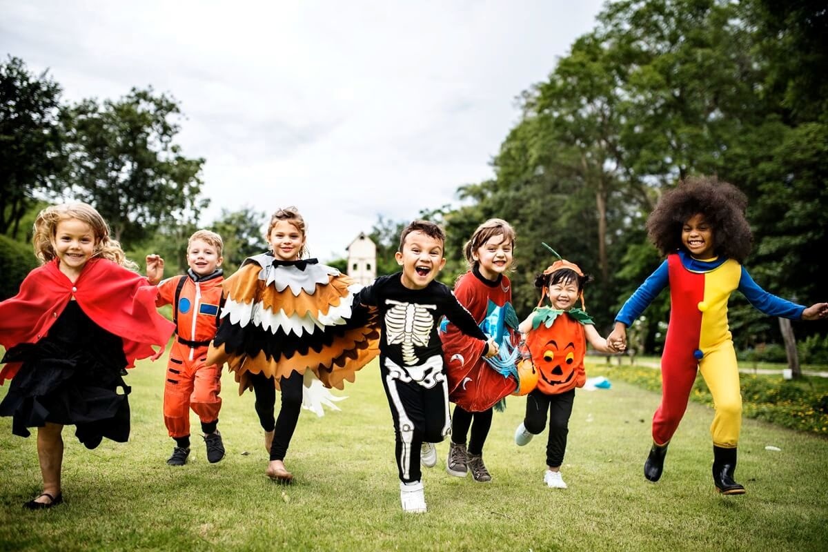 Copii alergând prin parc în costume de Halloween