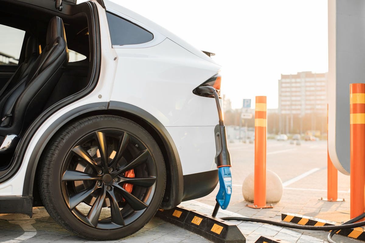 O mașină electrică albă, parcată și conectată la un încărcător într-o parcare exterioară