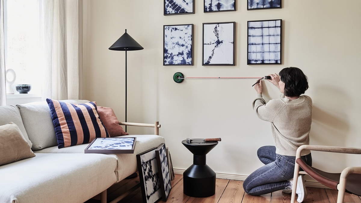 Žena věšící obrazy v obýváku s pomocí Atina