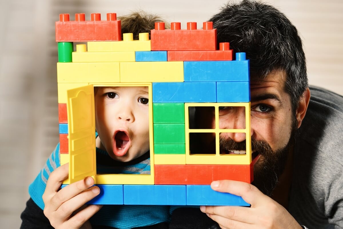 Баща и син гледат заедно през вратата и прозореца на къща от Лего