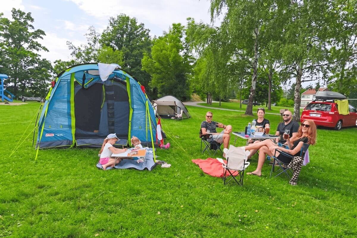 Kempingezők pihennek az összecsukható székeken egy tágas, négyszemélyes Coleman Castle Pines 4 családi sátor előtt.