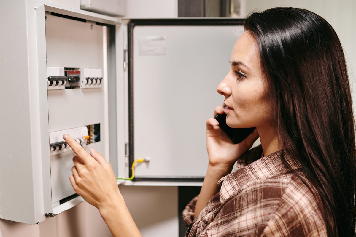 Mladá žena kontroluje elektrické jističe a telefonuje při tom Mladá žena kontroluje elektrické jističe a telefonuje při tom